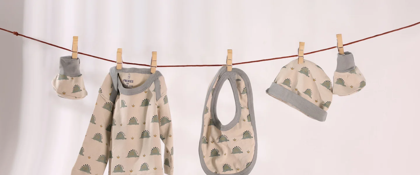 Baby bodysuit, bib, hat and booties clipped to a clothesline against a pale background