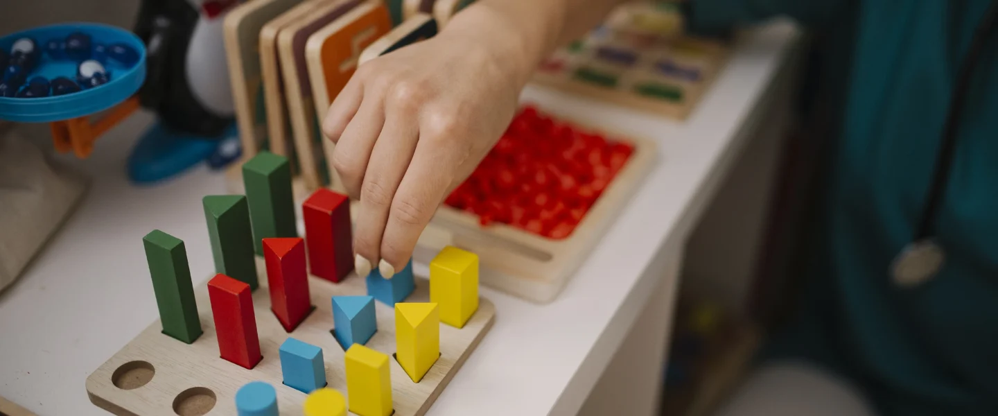 Child's hand placing colorful wooden shapes into a sorting board on a play table
