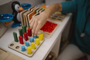 Child's hand placing colorful wooden shapes into a sorting board on a play table