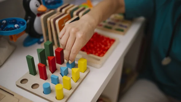 Child's hand placing colorful wooden shapes into a sorting board on a play table