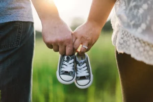 Two adults holding a tiny pair of dark canvas baby sneakers outdoors
