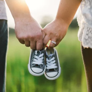 Two adults holding a tiny pair of dark canvas baby sneakers outdoors