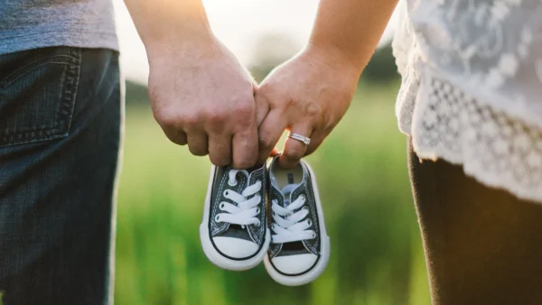 Two adults holding a tiny pair of dark canvas baby sneakers outdoors
